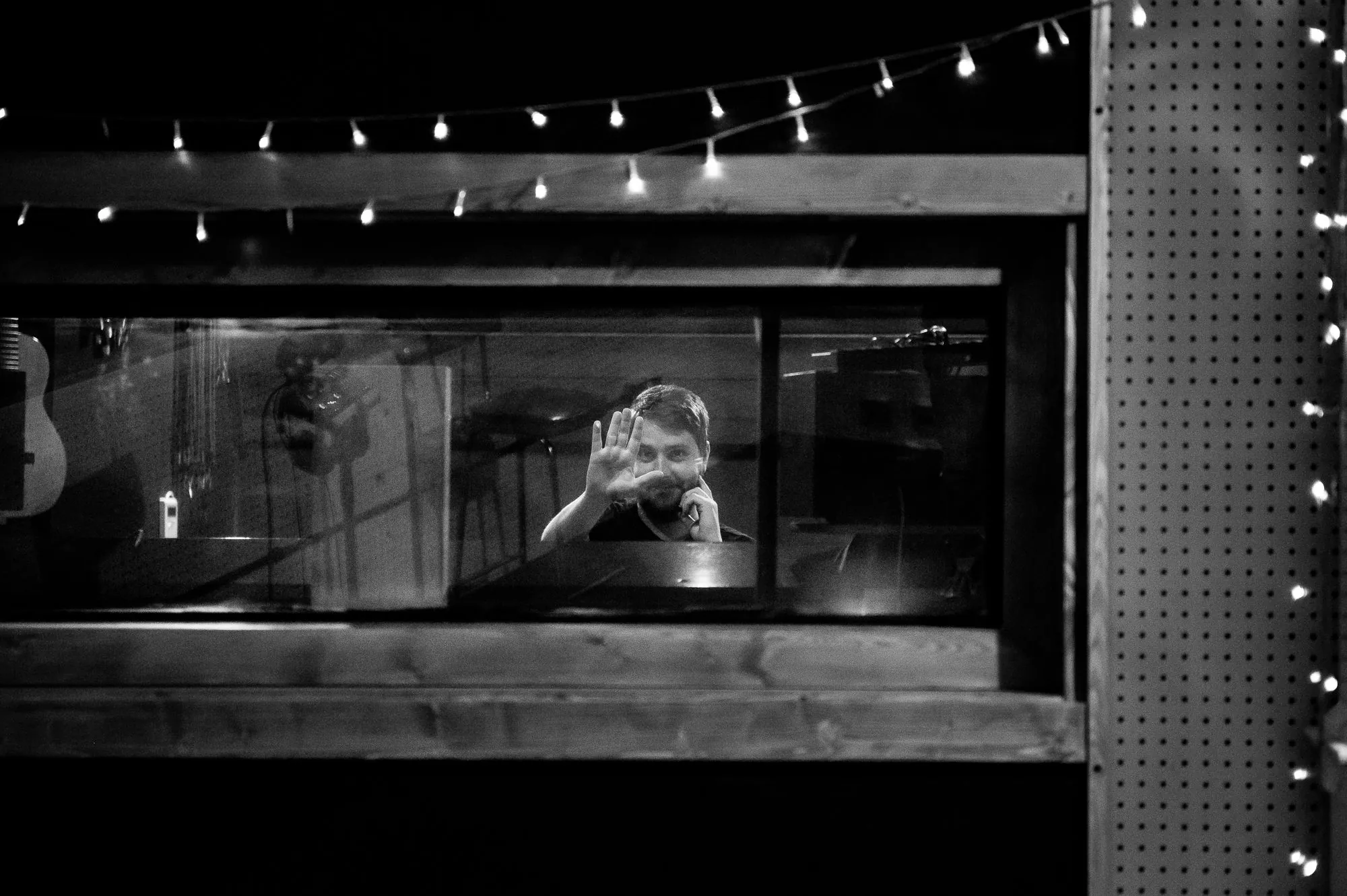 Elliot Vaughan waving through the control room glass, fairy lights strung above the window